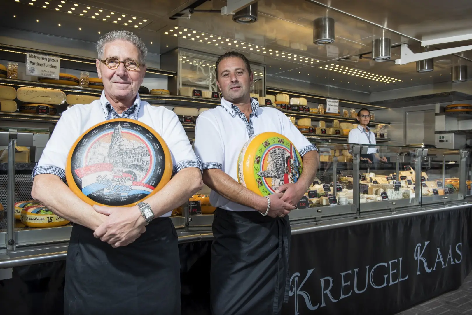 Twee vakmannen met een grote kaas in hun kaasspeciaalzaak